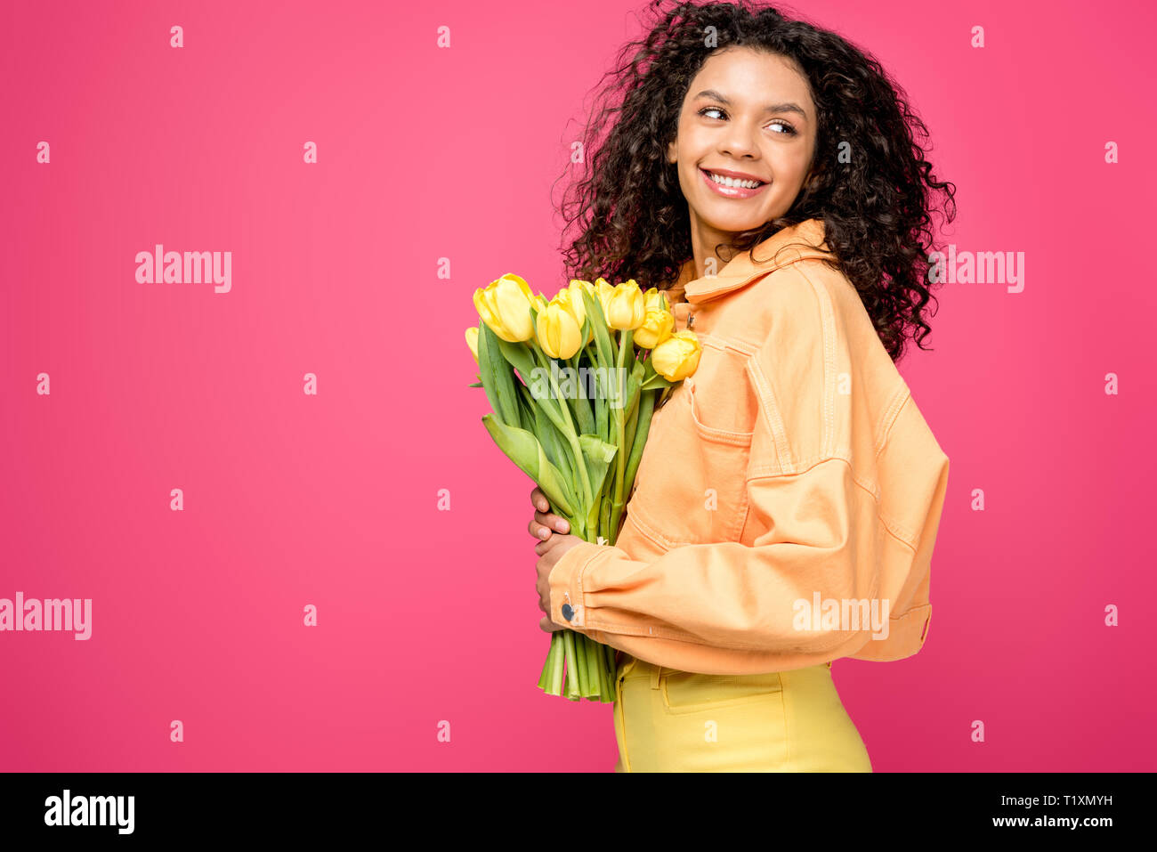 cheerful african american woman holding yellow tulips isolated on crimson Stock Photo