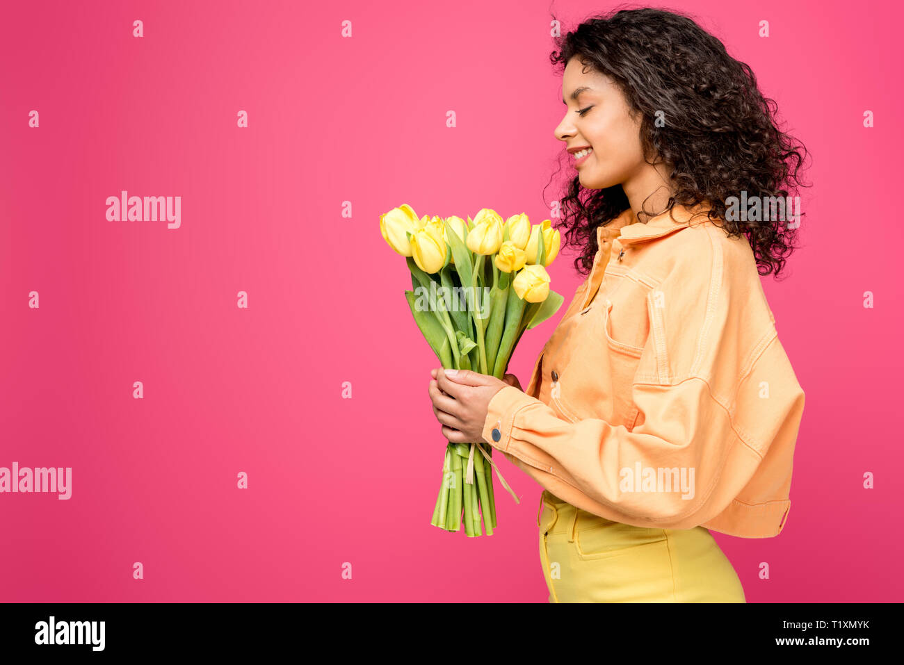 cheerful african american woman looking at yellow tulips isolated on crimson Stock Photo
