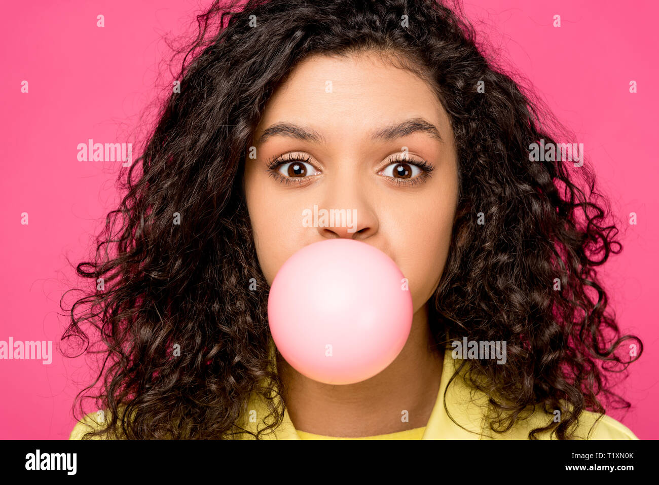 surprised curly african american girl blowing bubble gum isolated on crimson Stock Photo