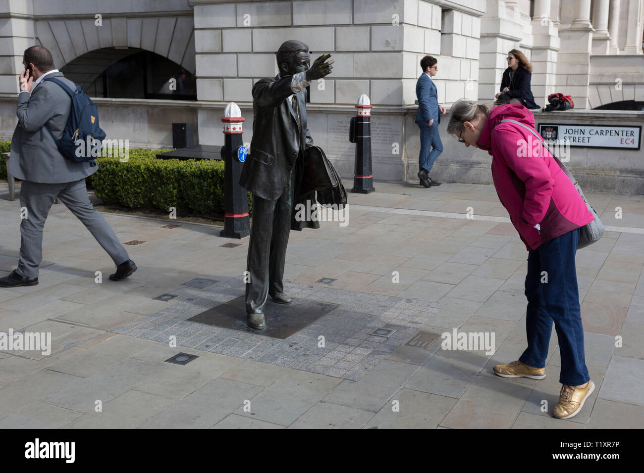 A passer-by studies the details of artist John Seward Johnson's sculpture, entitled 'Taxi!' (1983) on John Carpenter Street in the City of London, the capital's financial district, on 25th March 2019, in London, England. Stock Photo