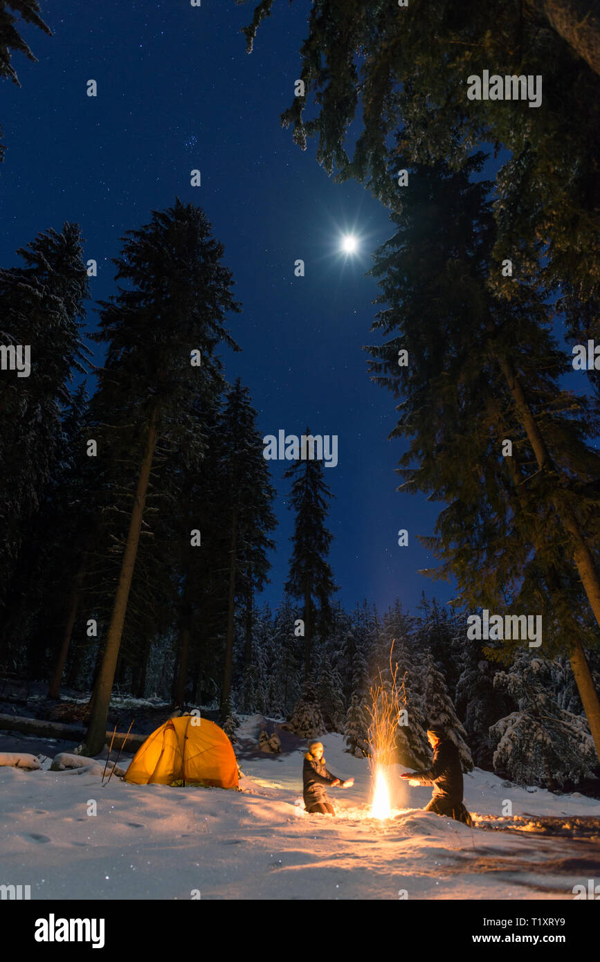 couple camping with campfire and tent outdoors in winter Stock Photo