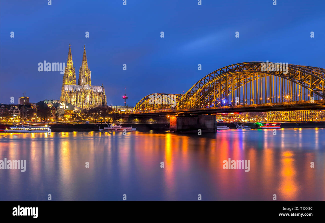 An evening view of the Cologne Cathedral over the Rhine river, with the Hohenzollern railway bridge in the foreground, Cologne, Germany Stock Photo