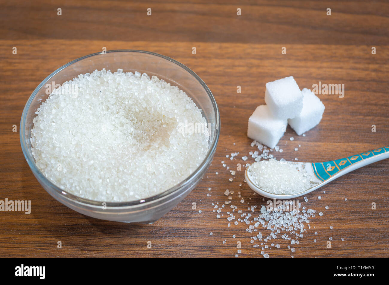 White sugar kept in a glass bowl with a spoon. Some sugar cubes kept on