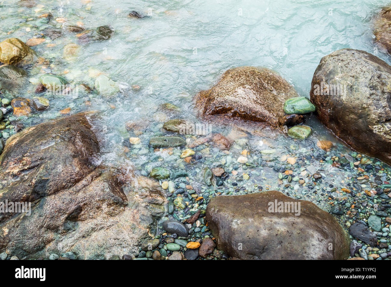 Boulders and pebbles on the bank of a river with milky green colour water Stock Photo
