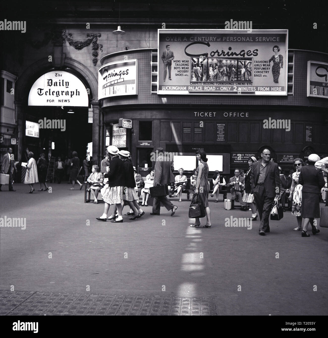 1960, historical, Victoria train station, London, showing commuters, ticket office and promotional billboards, with adverts for the Daily Telegraph daily newspaper and for the department store Gorringes in Buckingham Palace Road, advertising over 100 years of personal service. Frederick Gorringe opened a small drapery store there in 1858 and it became a well-known, fashionable store until its closure in 1968. Stock Photo