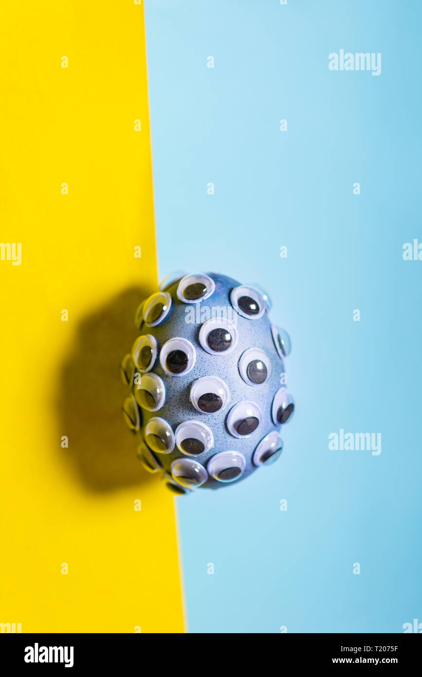 Blue egg shell covered with googly eyes on bright yellow and blue