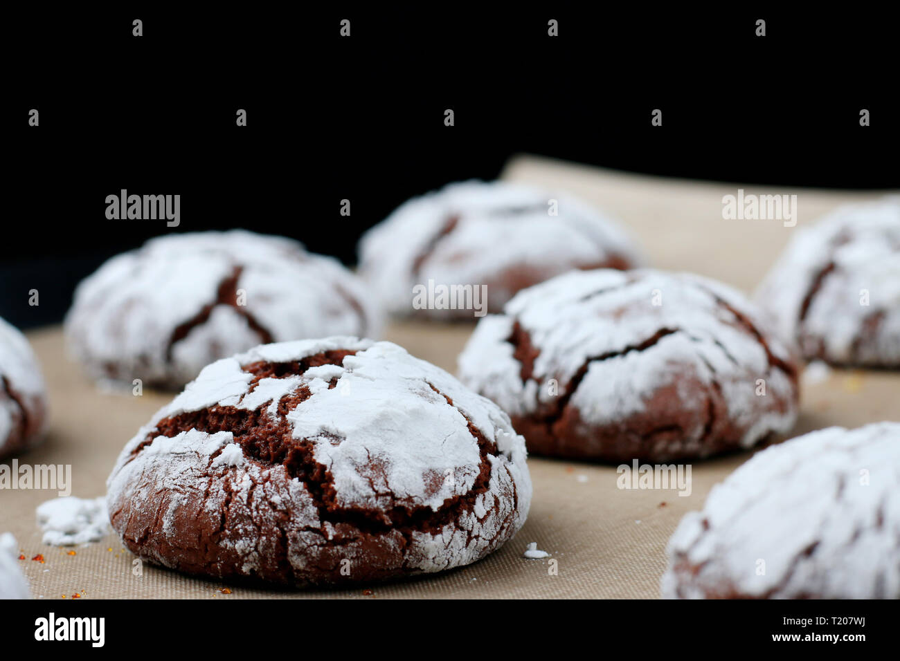 Chocolate cookies with cracks on baking paper and iolated on black. Cracked chocolate biscuits. Stock Photo