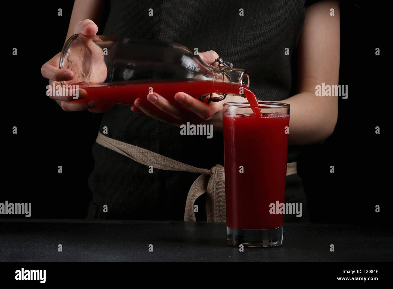 girl pouring juice in glass on dark background. summer drink concept
