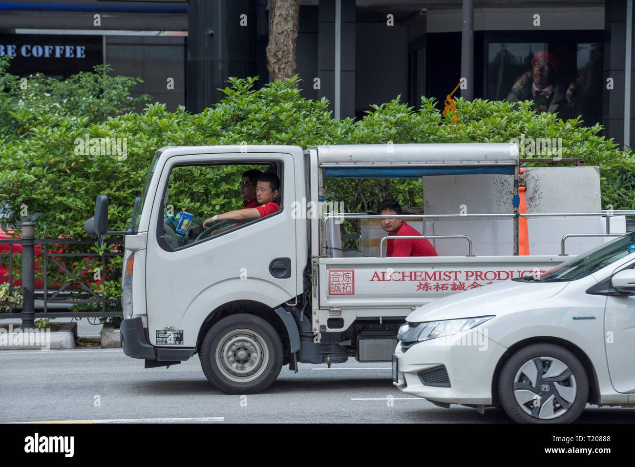 A work truck waits in Singapore traffic with two people in front seats and a third person in the back tray Stock Photo
