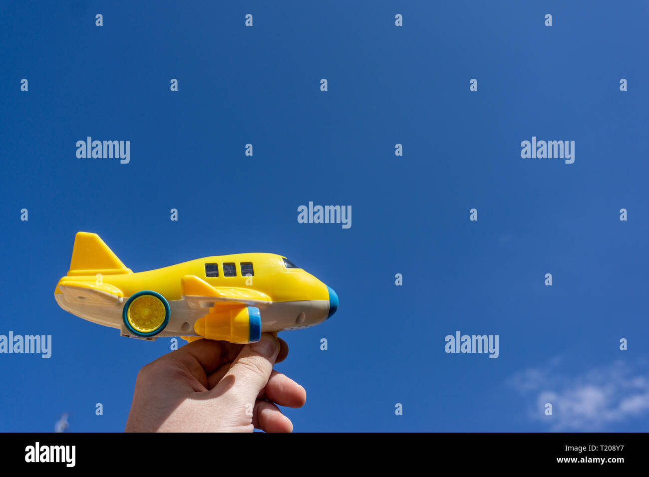 Yellow toy plane flying in to the beautiful blue sky, negative space, concept of going on a magical holiday, dream destination Stock Photo