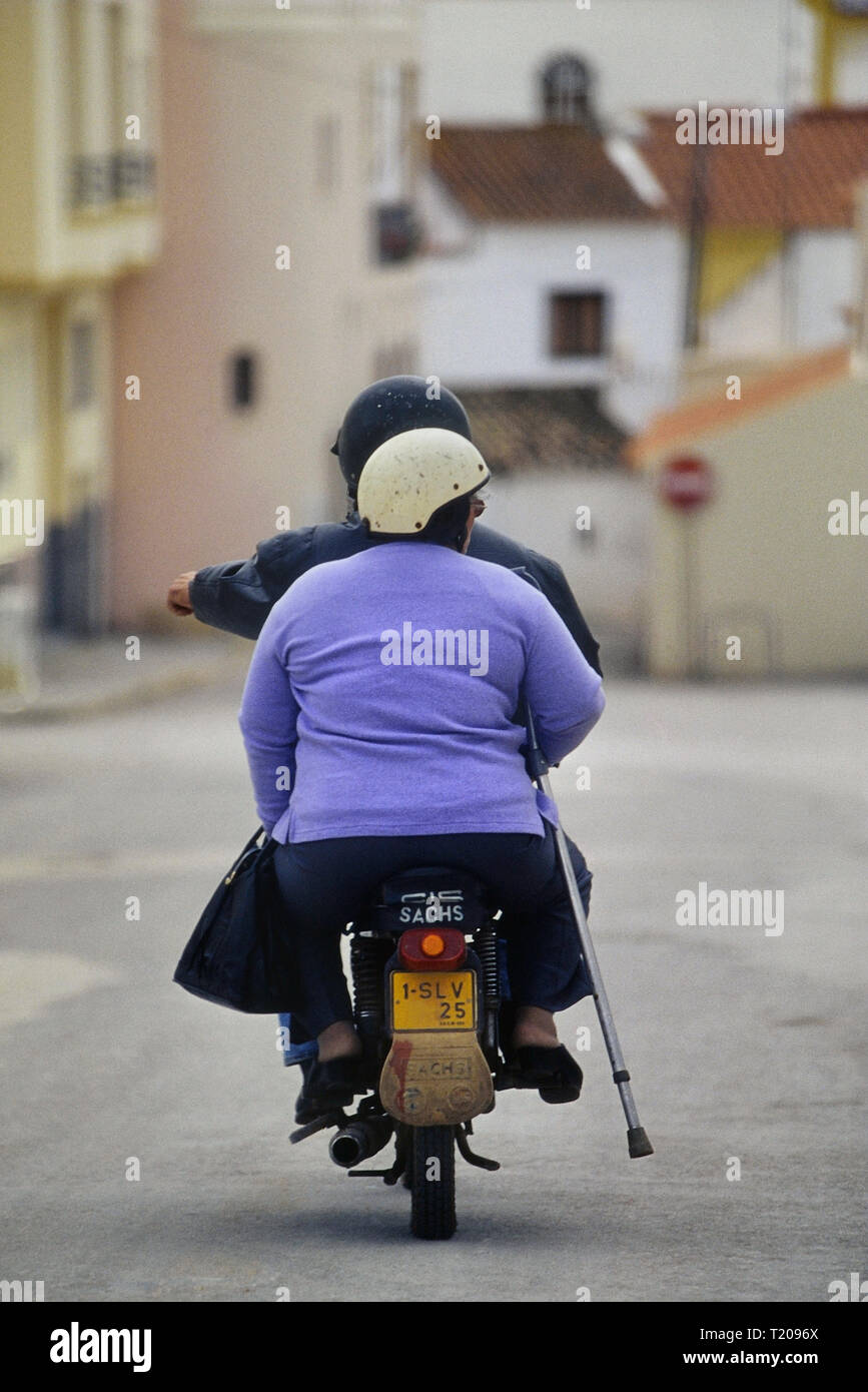A disabled woman passenger with a crutch riding on the back of a motor scooter. Portugal. Stock Photo