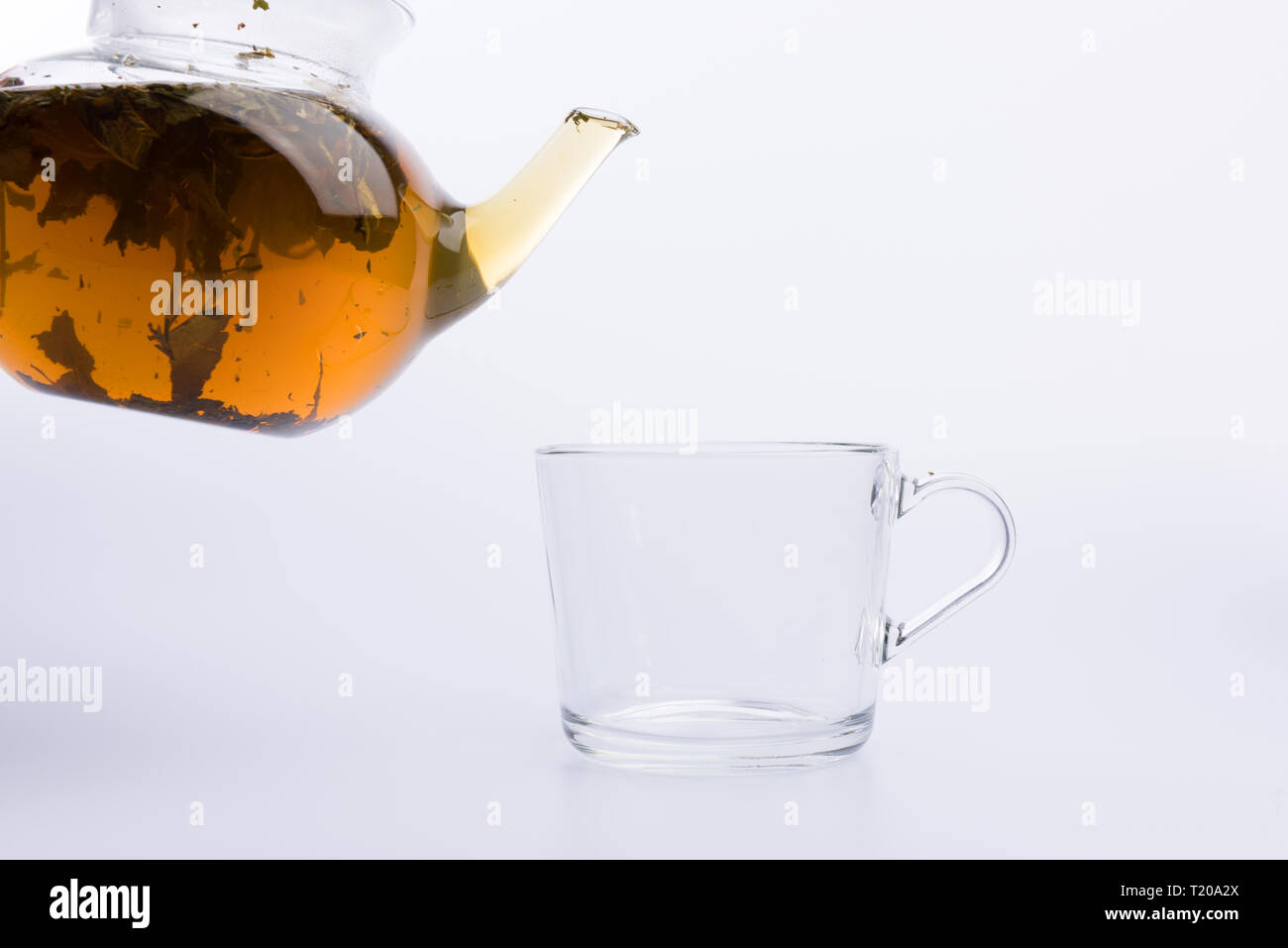 Glass teapot pouring green tea into cup isolated on white Stock Photo