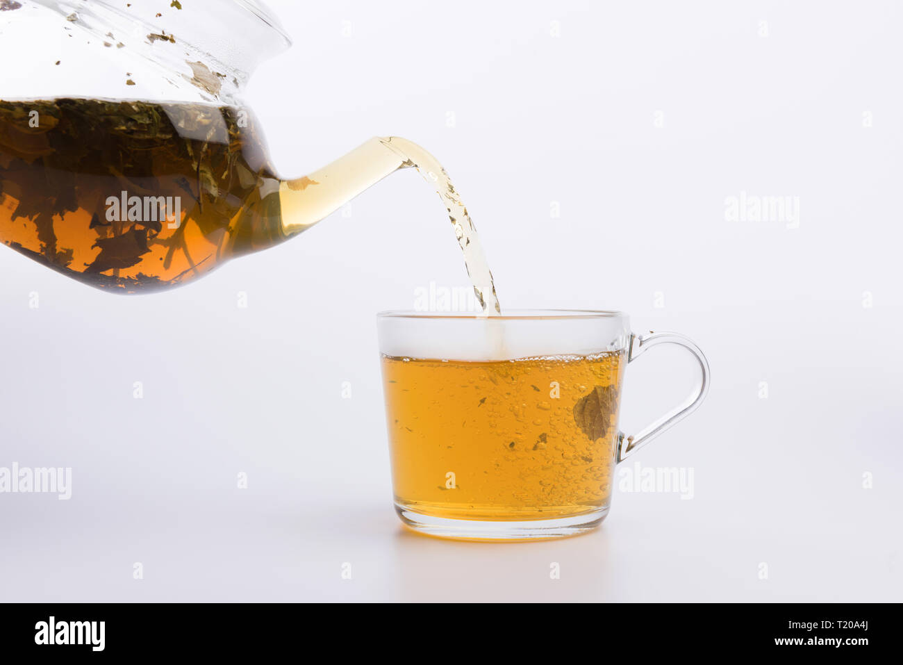 Glass teapot pouring green tea into cup isolated on white Stock Photo