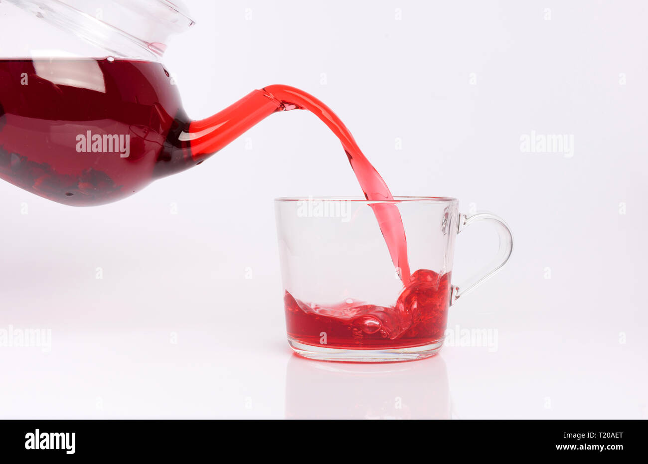 Glass teapot pouring hibiscus tea into cup isolated on white Stock