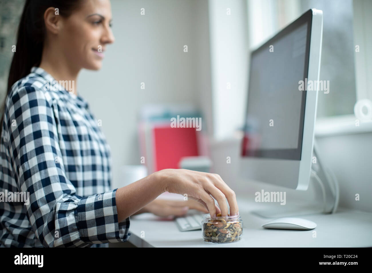 Female Worker In Office Having Healthy Snack Of Dried Nuts And Seeds Stock Photo