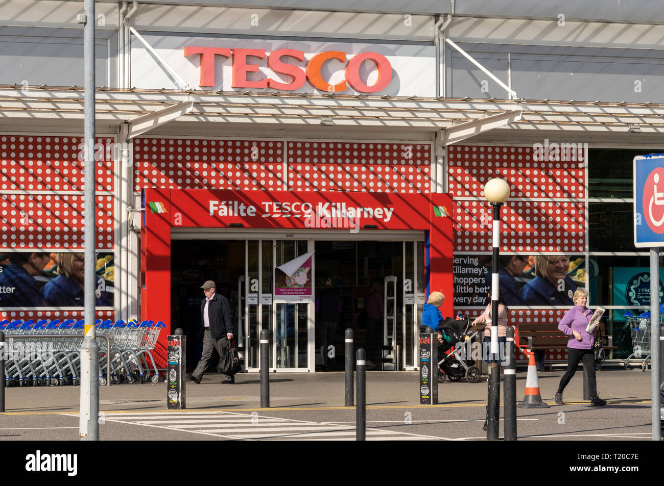 Tesco logo unusual bright red entrance. Customers at Tesco red store front in Killarney DeerPark shopping centre on sunny day. Killarney  County Kerry Stock Photo