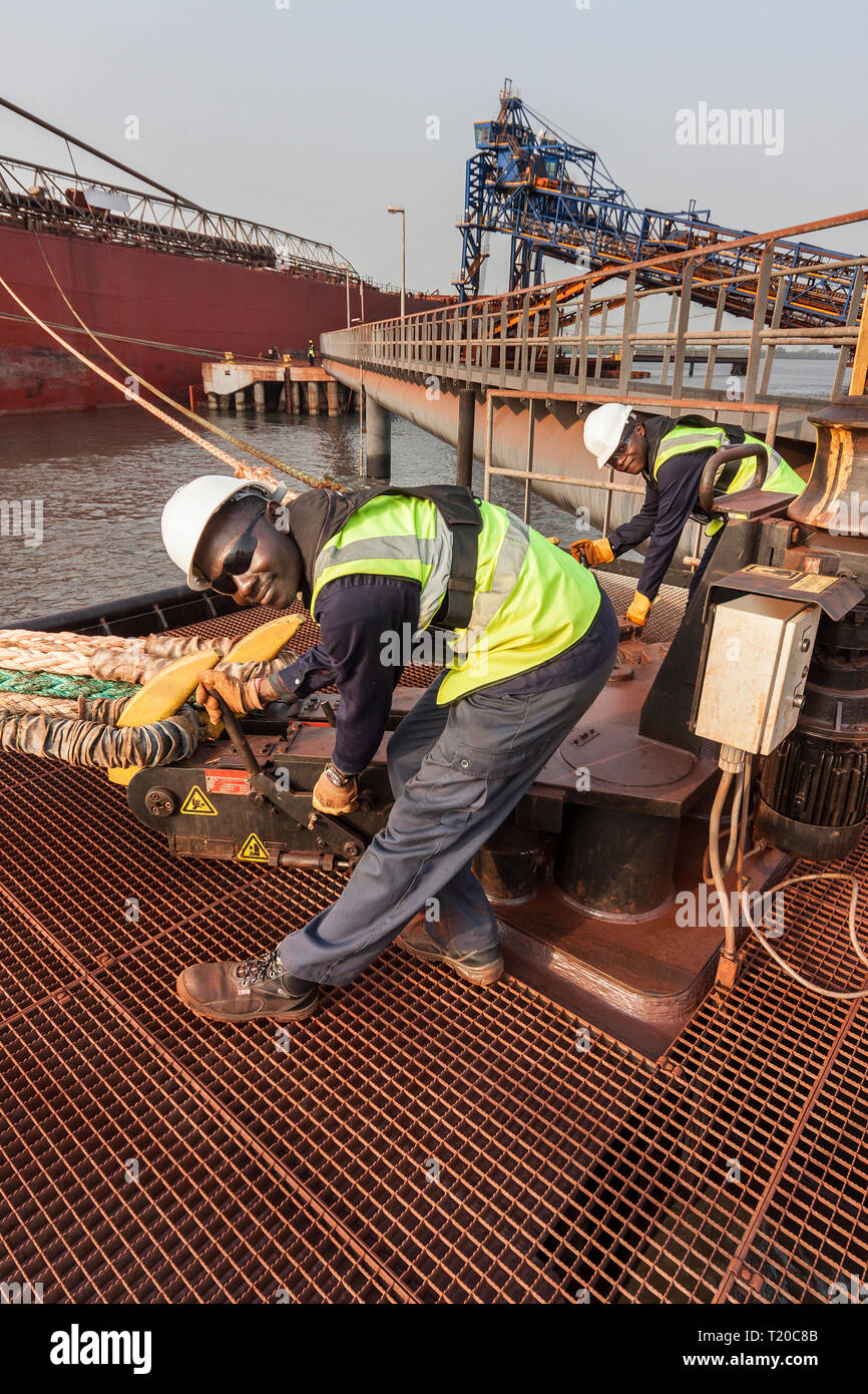 Port operations for managing and transporting iron ore.  Dolphin jetty mooring facility with riggers using quick release rope hooks as ship sets sail Stock Photo