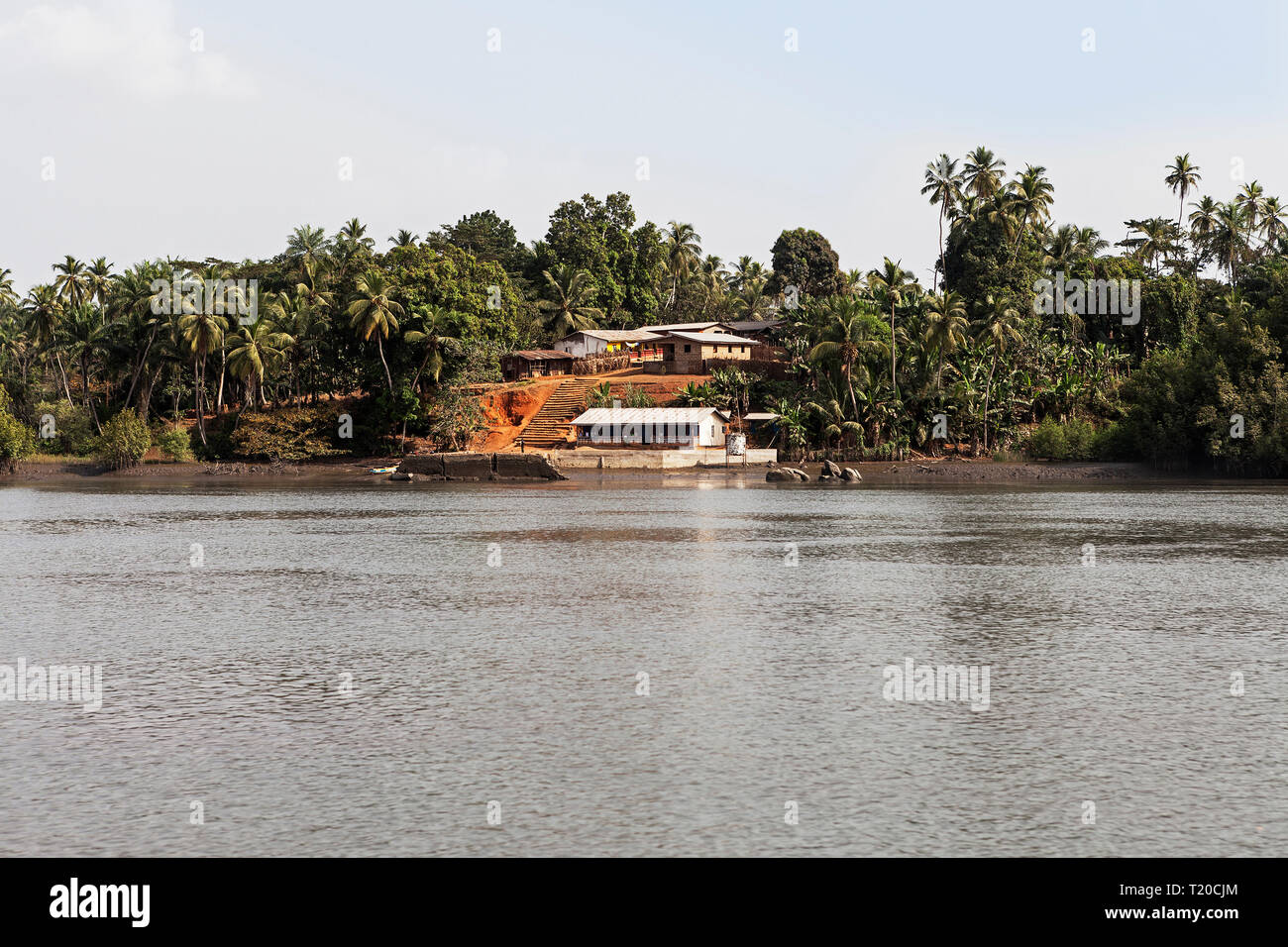 Lush tropical vegetation and African village up Port Loko Creek plus café restaurant at landing stage for small marine craft and boats, Sierra Leone Stock Photo