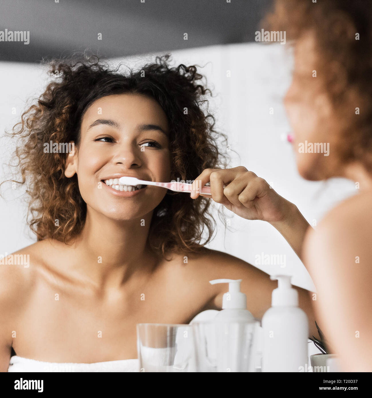 Smiling young afro woman with toothbrush cleaning teeth at bathroom