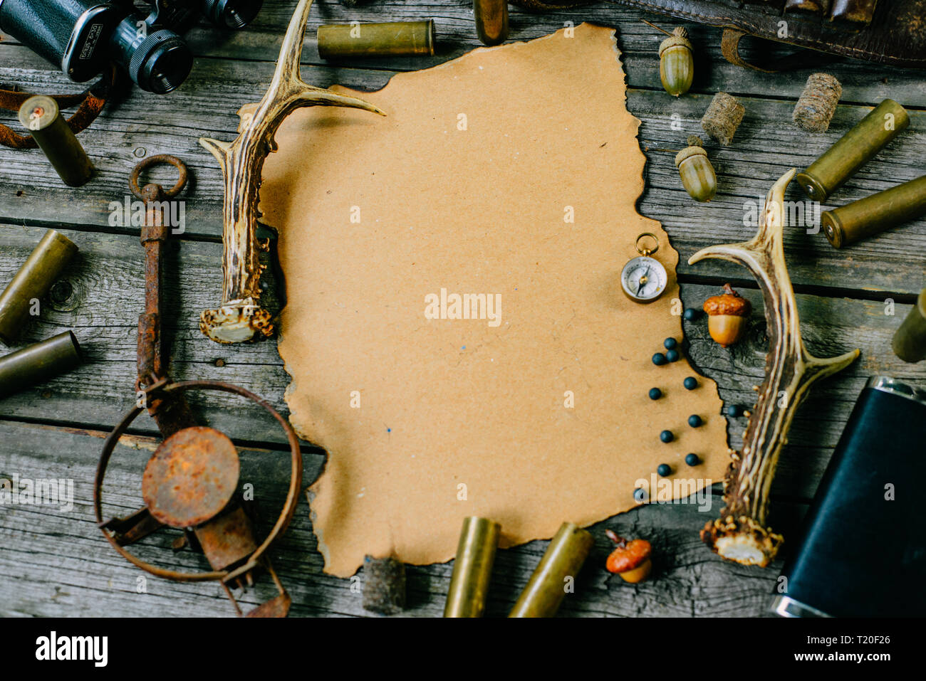 Paper for information with horn, trap and cartridges beside on old wooden background. Hunting equipment on vintage board. Stock Photo