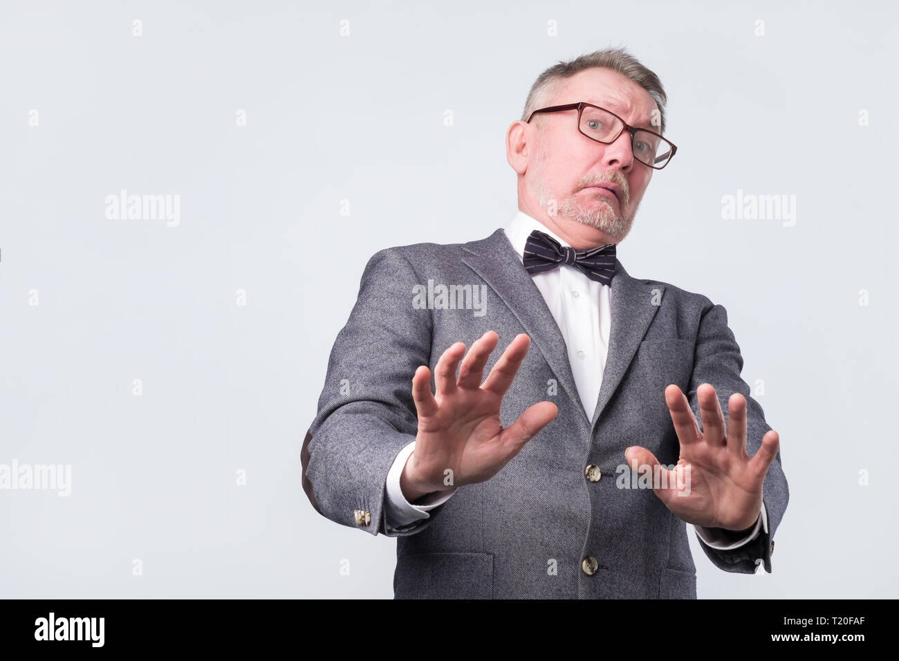Mature european man in suit and glasses showing refusal gesture. It is not for me, leave me in piece, has angry expression. Studio shoot Stock Photo