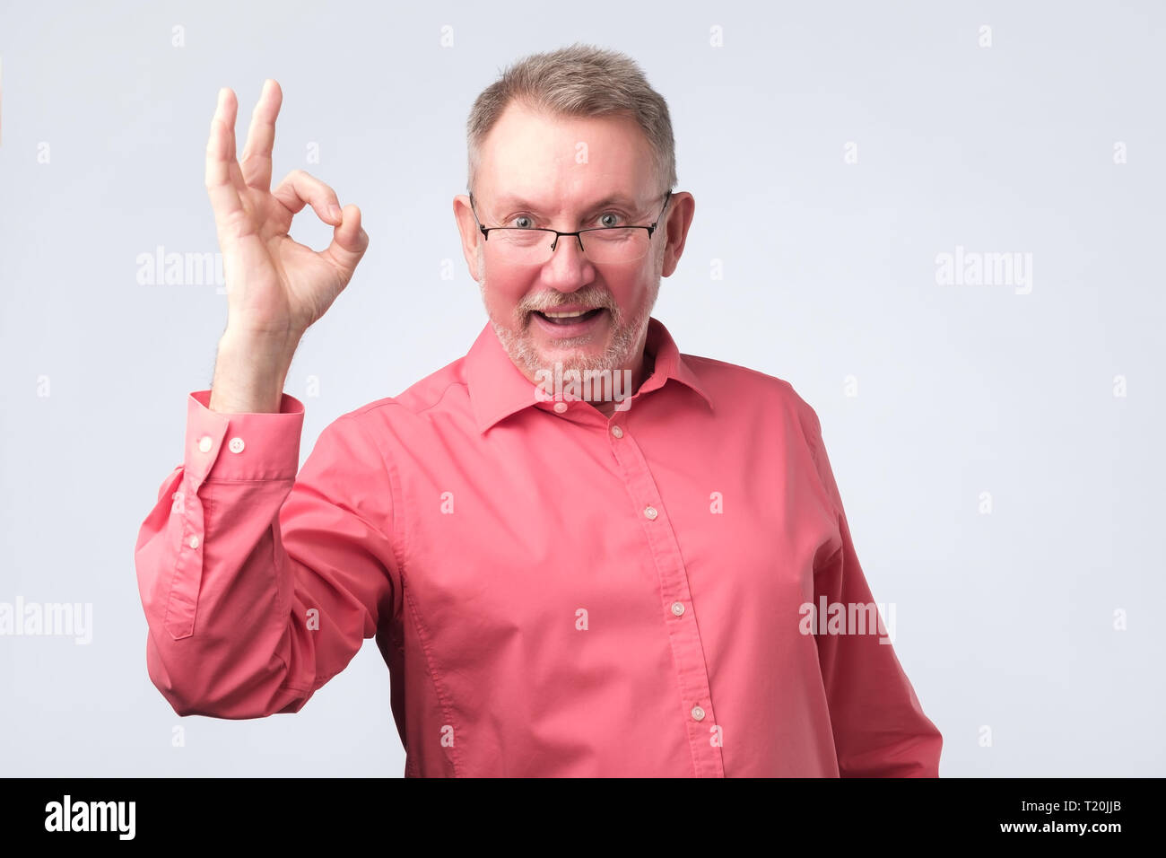Senior european man in red shirt showing OK sign. Approval of your choice concept Stock Photo