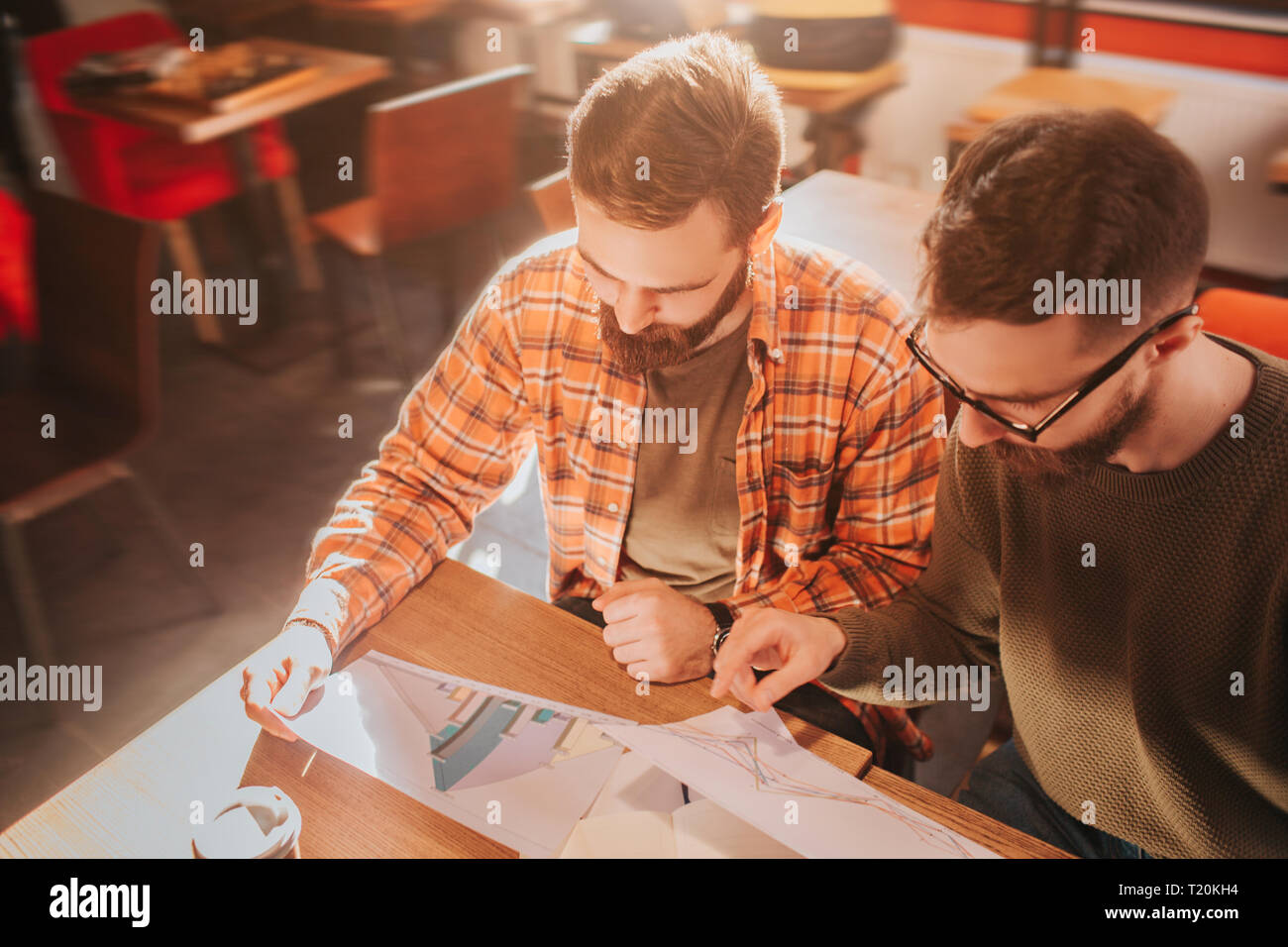 Close up of two adult and bearded guys sitting at the table and studying graphics in documents. They are preparing for demonstation this materials Stock Photo