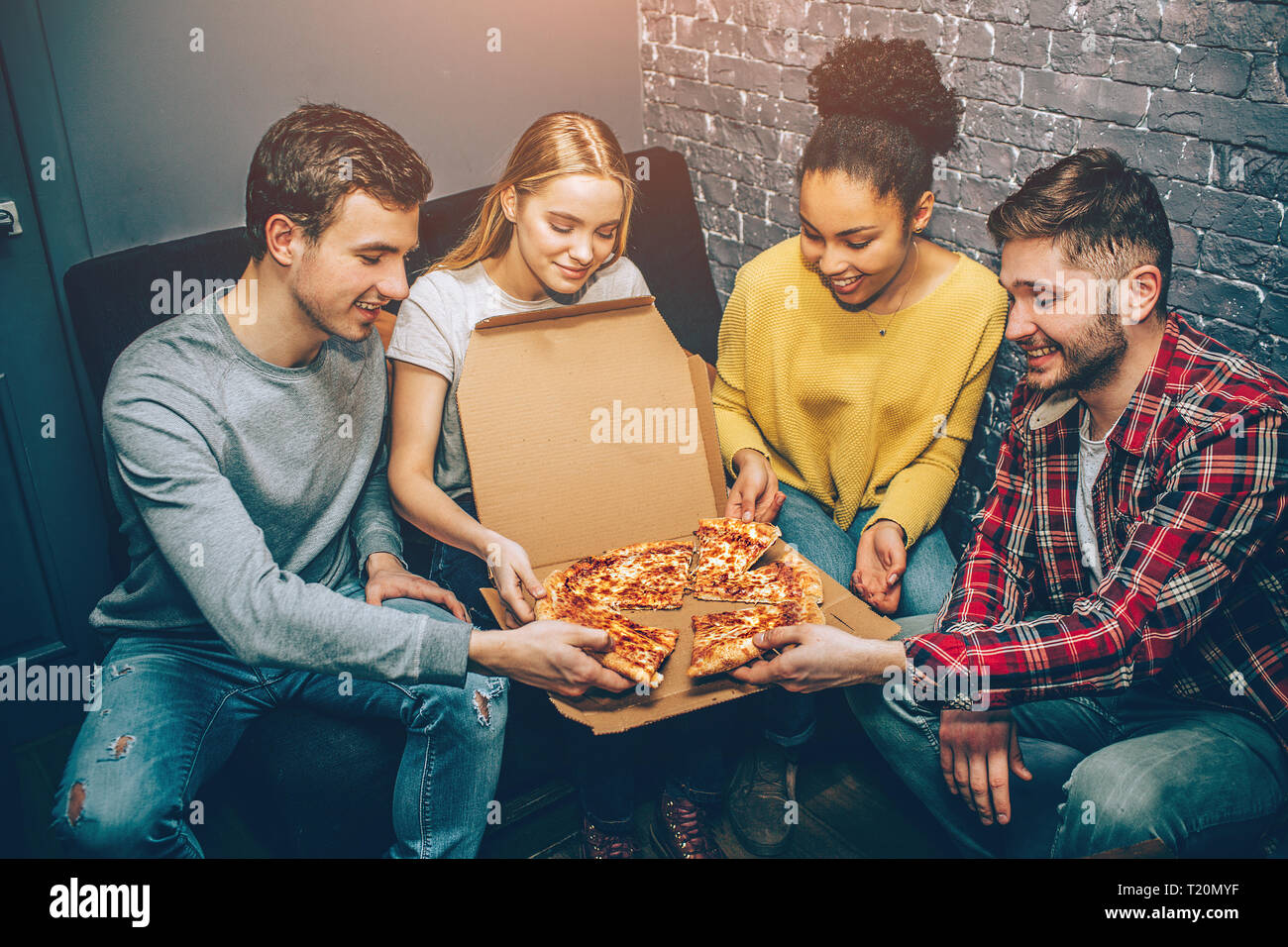 Group picture of students where everybody is holding a peace of pizza. They are so hungry that they can't wait anymore and want to eat it right now. P Stock Photo