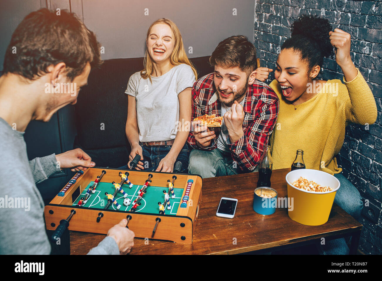 A shot where boys are playing football board game on the table while girls are cheering. Everybody is happy thinking only about the game Stock Photo