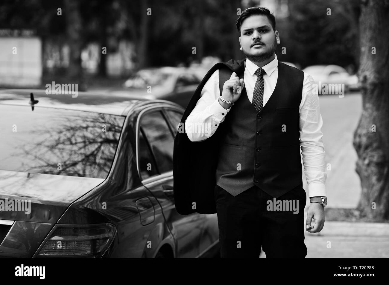 Stylish indian businessman in formal wear standing against black business car on street of city. Stock Photo