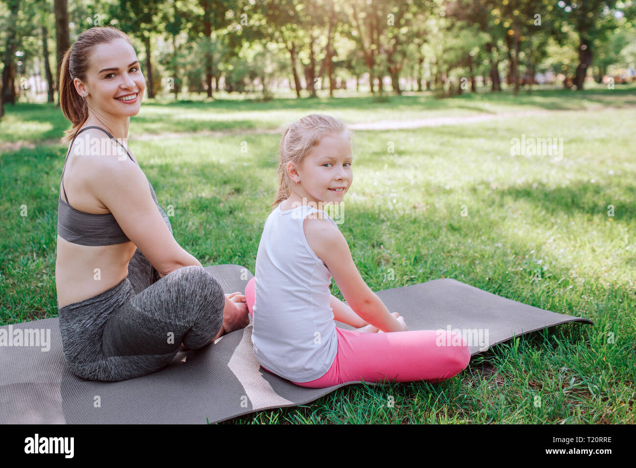 Nice girls are sitting together on carimate in lotus position and looking on camera. They are happy. Girls are smiling Stock Photo