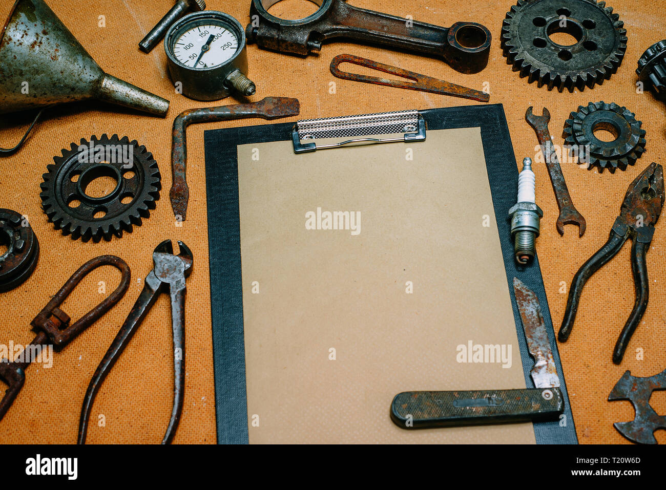Clipboard with paper for your info in the center of rusty tools, gears on vintage fiberboard background. Motorcycle equipment and repair template. Stock Photo