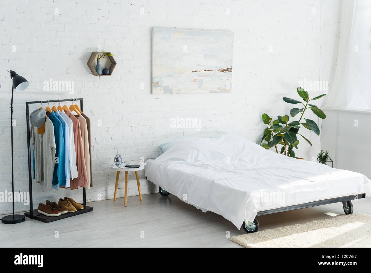 bed, clothes rack with shirts, plant, floor lamp and coffee table in