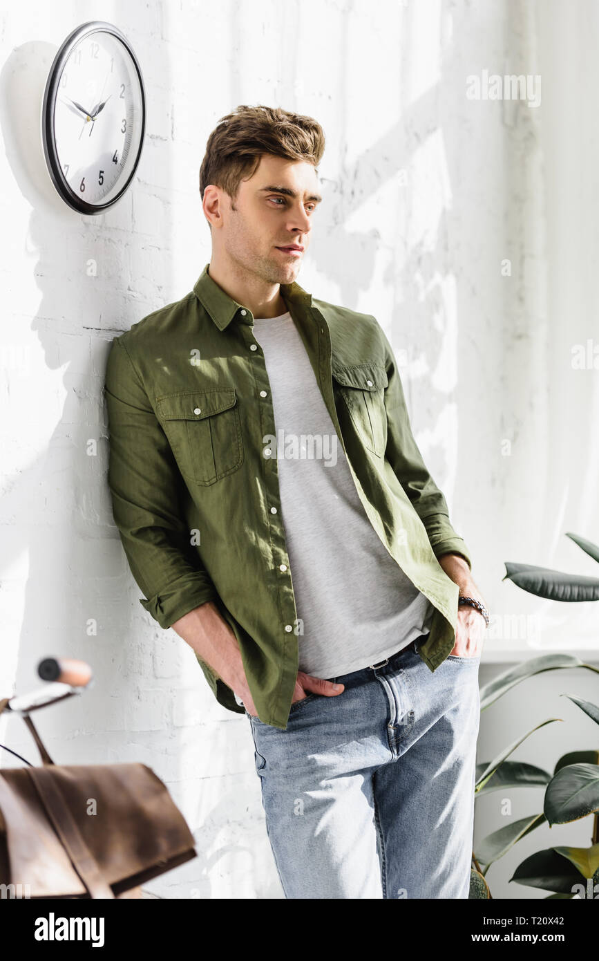 handsome man in green shirt and jeans standing near brick wall clock and plants in office Stock Photo Alamy
