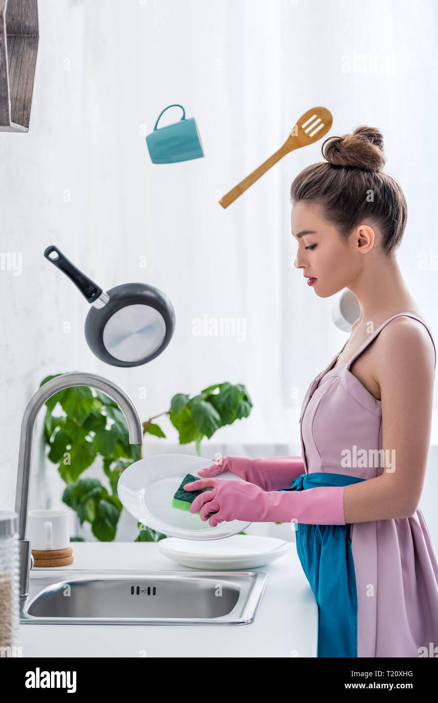 young woman in rubber gloves washing dishes while cooking utensils