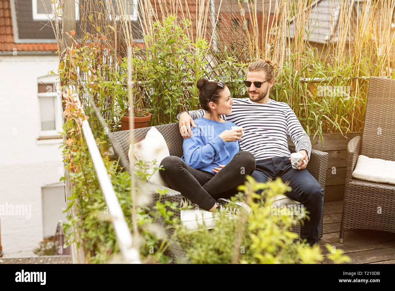 Young couple relaxing on their balcony, sitting on couch Stock Photo