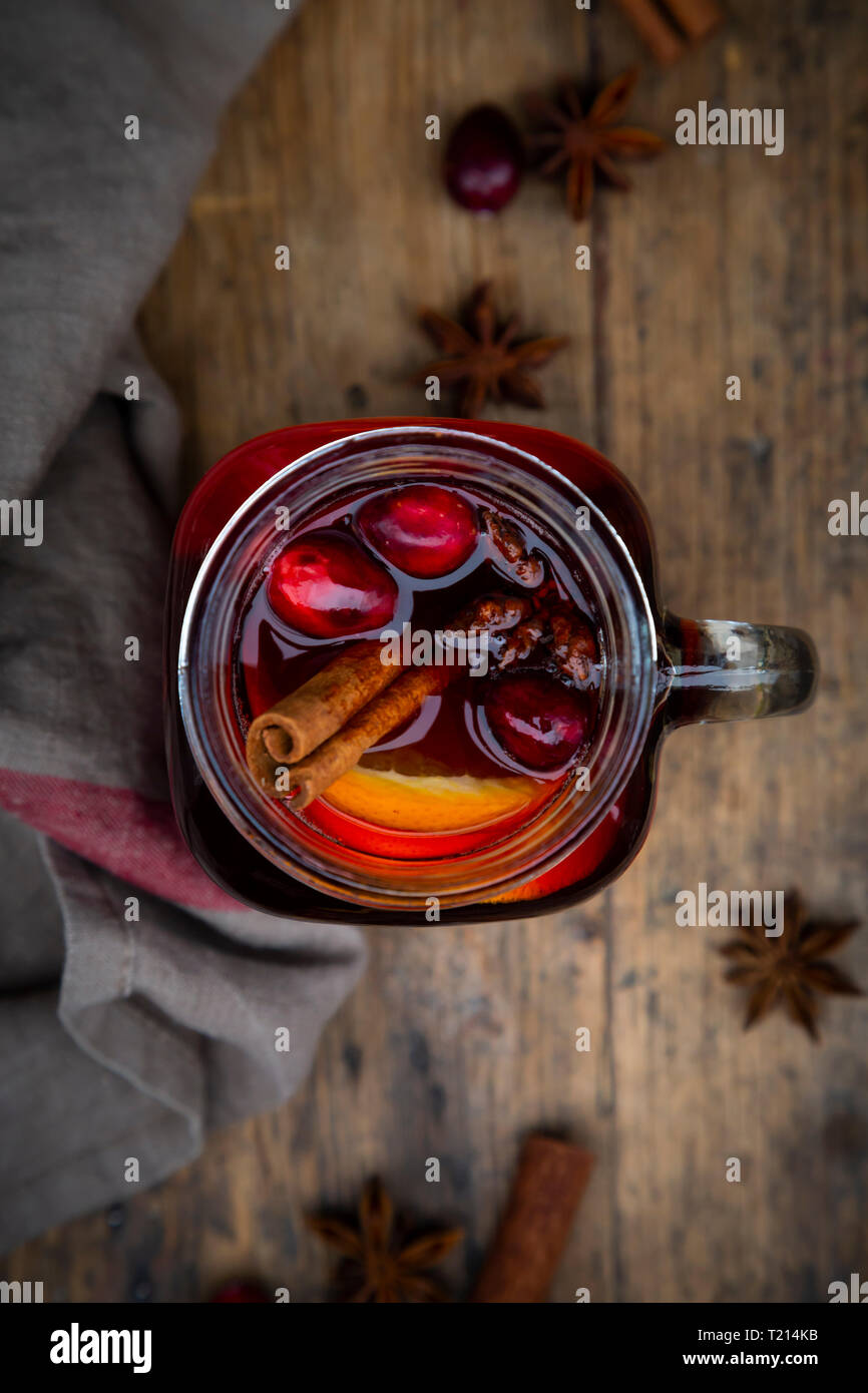 Glass of mulled wine with cranberries, cinnamon sticks, orange and star anise on dark wood, focus on foreground Stock Photo