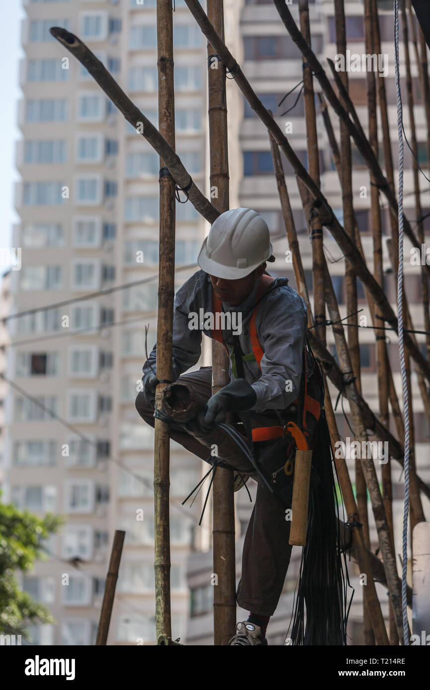 Construction worker fixing bamboo scaffolding on high rise construction site in city Stock Photo