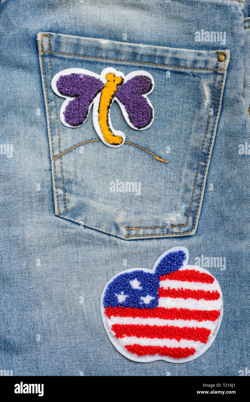 Applying fabric patches to denim. Butterfly and apple with American flag appliques. Trendy way to improve your jeans. Stock Photo