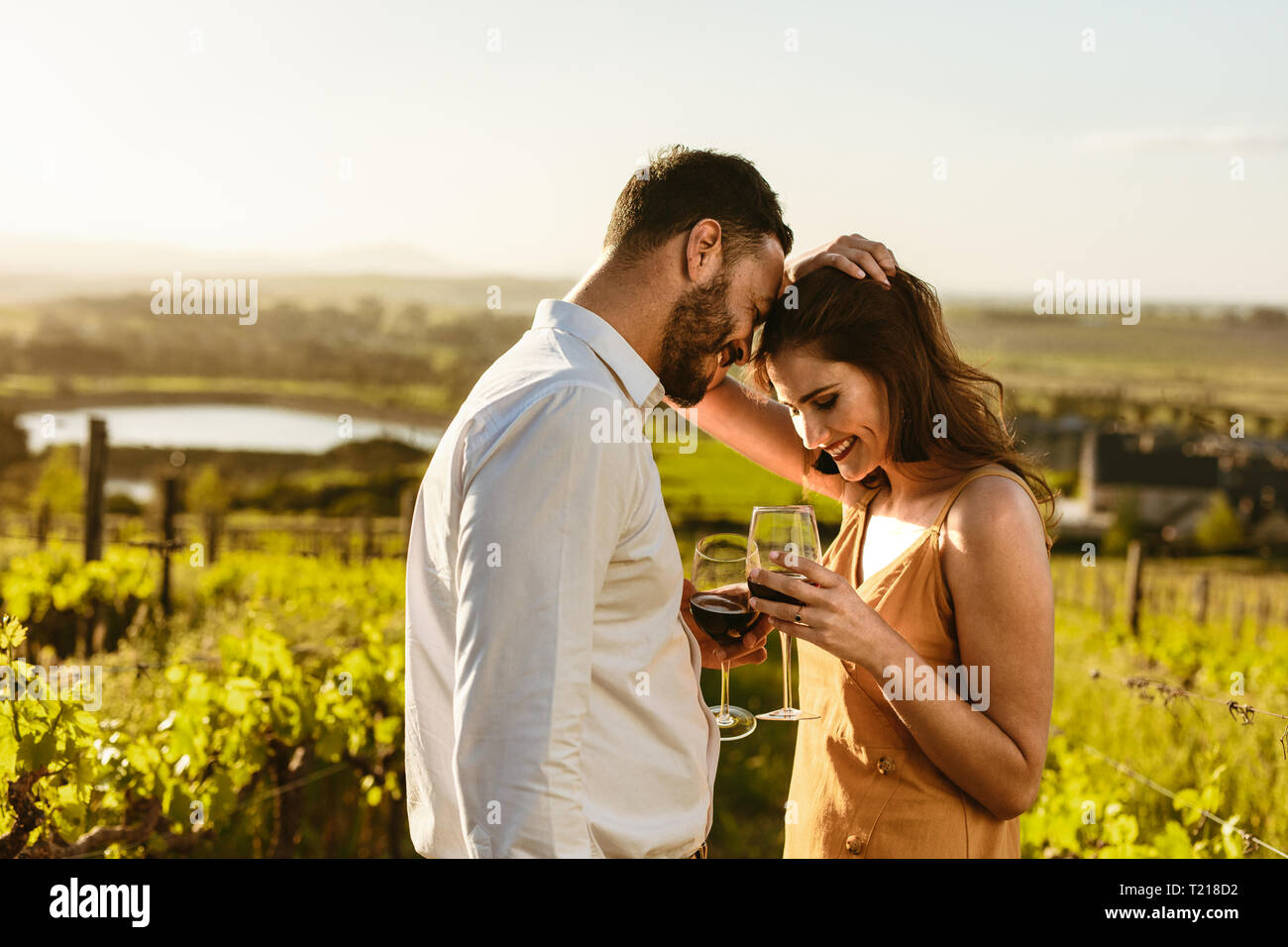 Couple on a romantic date standing together drinking red wine in a wine farm. Couple on a wine date spending time together. Stock Photo