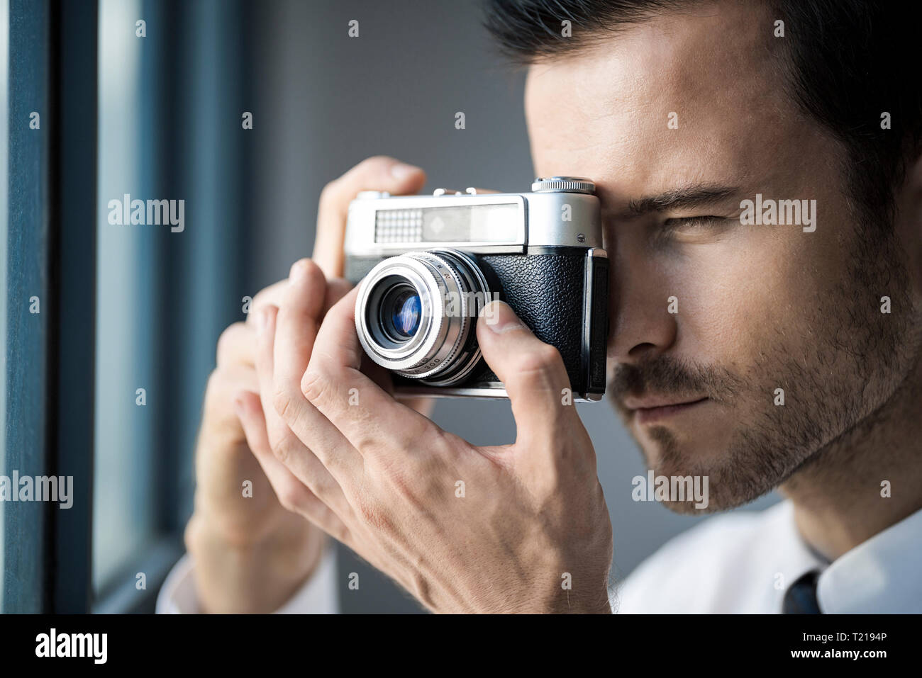 Close-up of businessman taking picture with vintage retro camera in front of office window Stock Photo