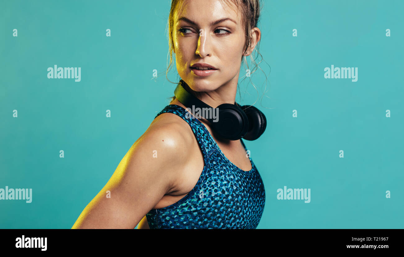fitness woman in sportswear and headphones looking over shoulder. Strong sports woman on blue background Stock Photo