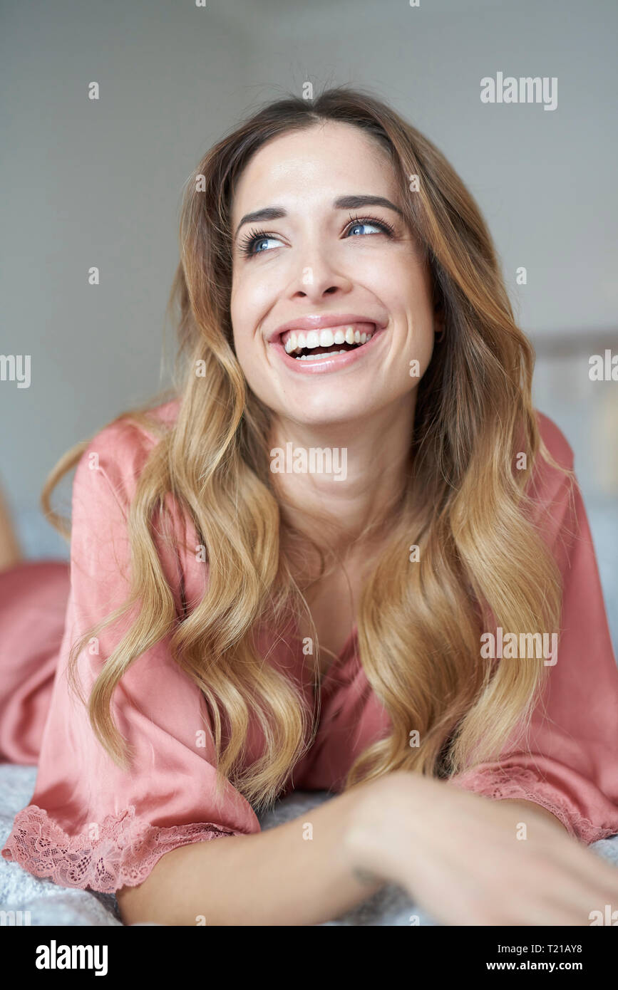 Laughing young woman in dressing gown lying in bed Stock Photo