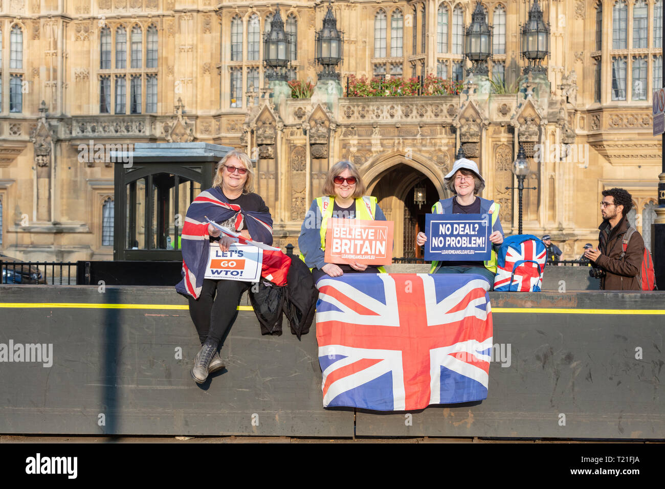 London, UK; 29th March 2019; Three Female Pro-Brexit Demonstrators Sit on Security Barrier Outside Parliament Holding Pro-Brexit Signs and union Jack Flag. Stock Photo