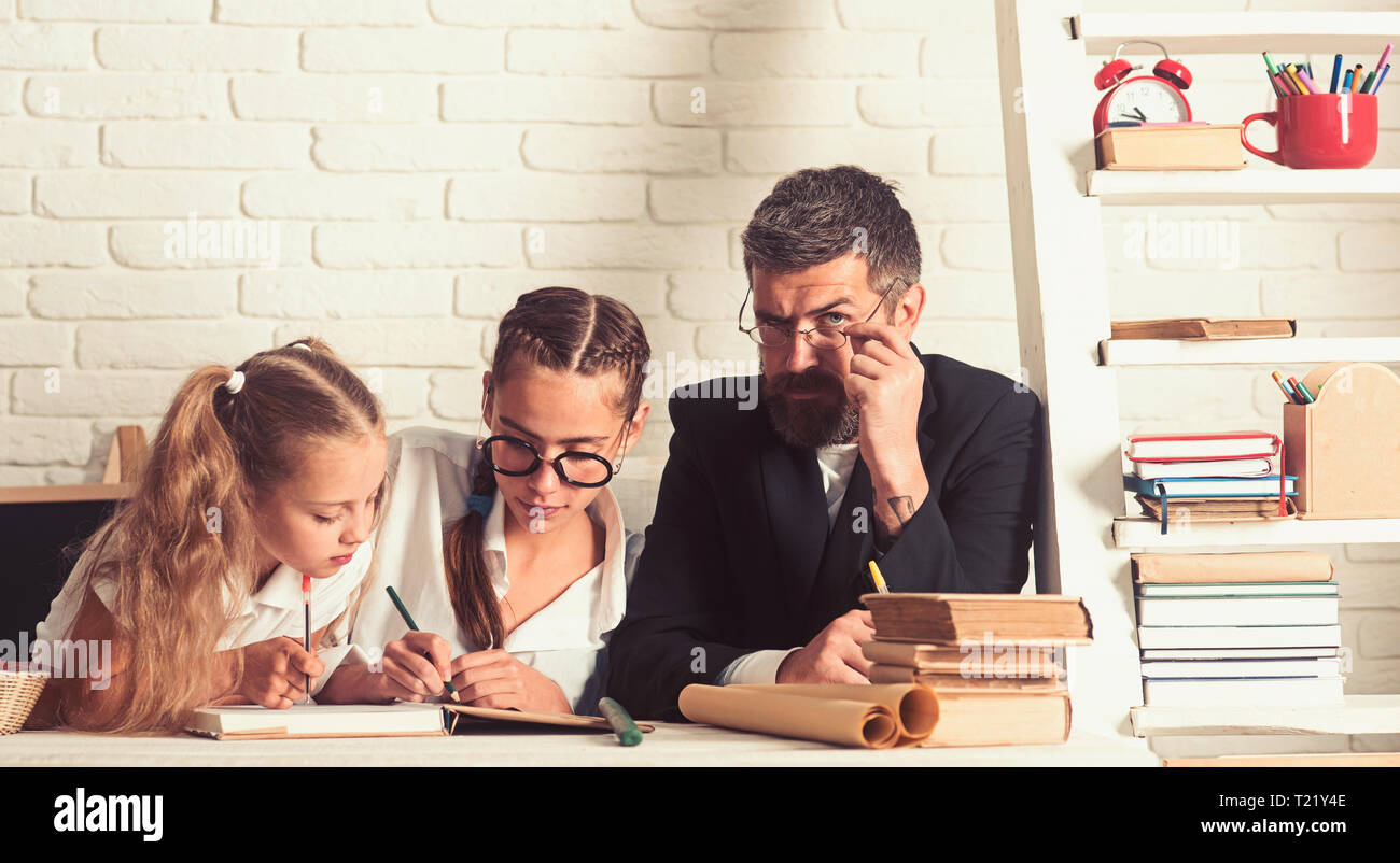 Education and knowledge day. Back to school and home schooling. Father helps children to study at home. School time of girl sisters with father Stock Photo