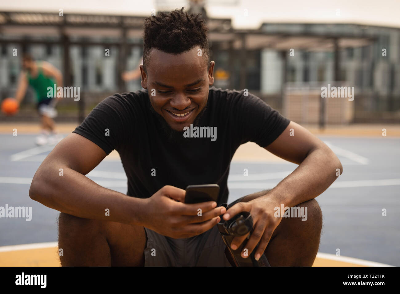 Basketball player sitting on a basketball while he is using mobile phone Stock Photo