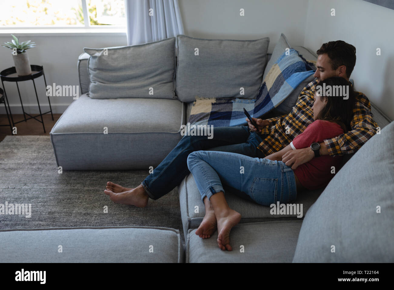 Couple using mobile phone while leaning on sofa at home Stock Photo