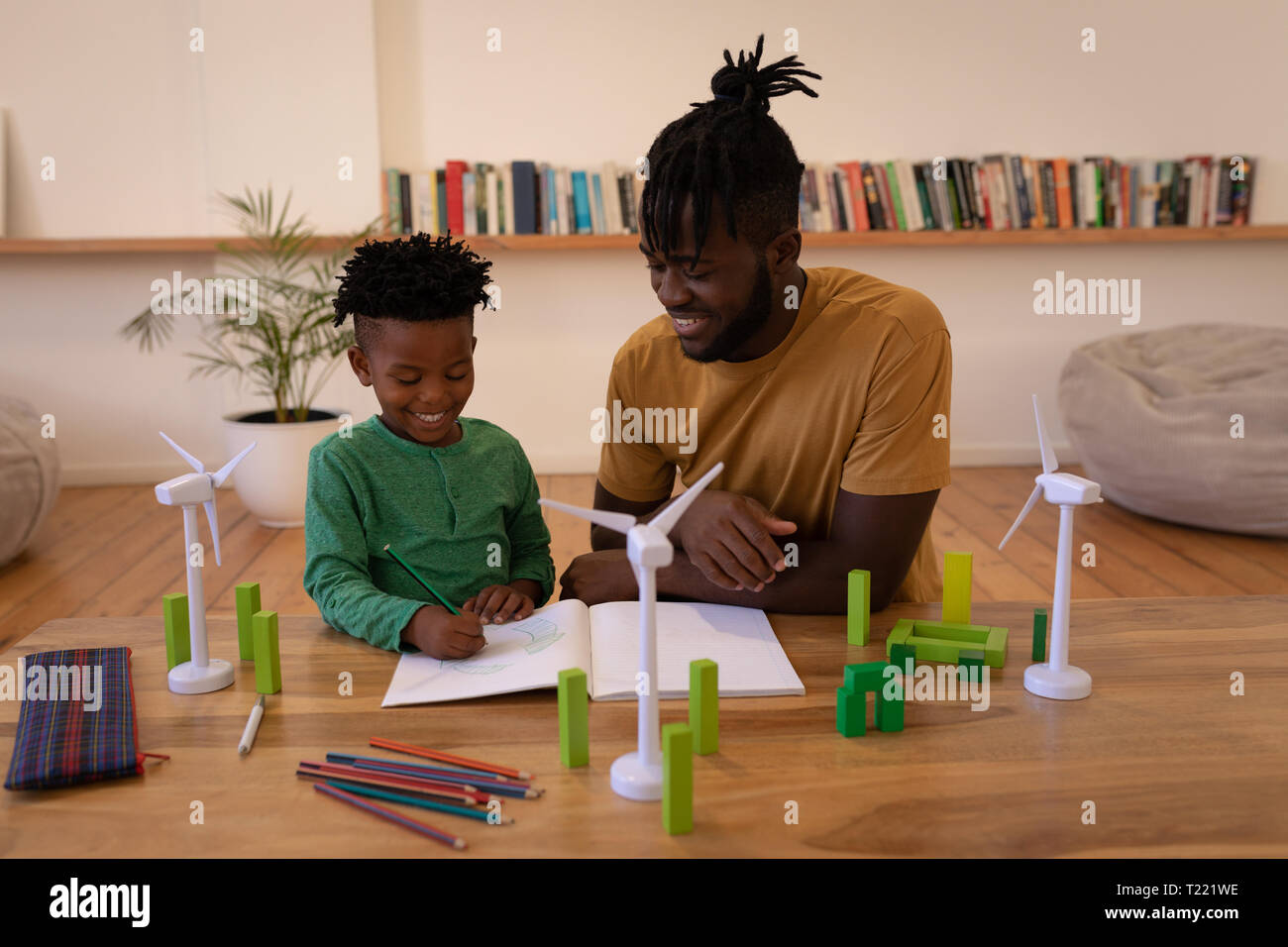 Father assisting his son in drawing while sitting on chair at home Stock Photo