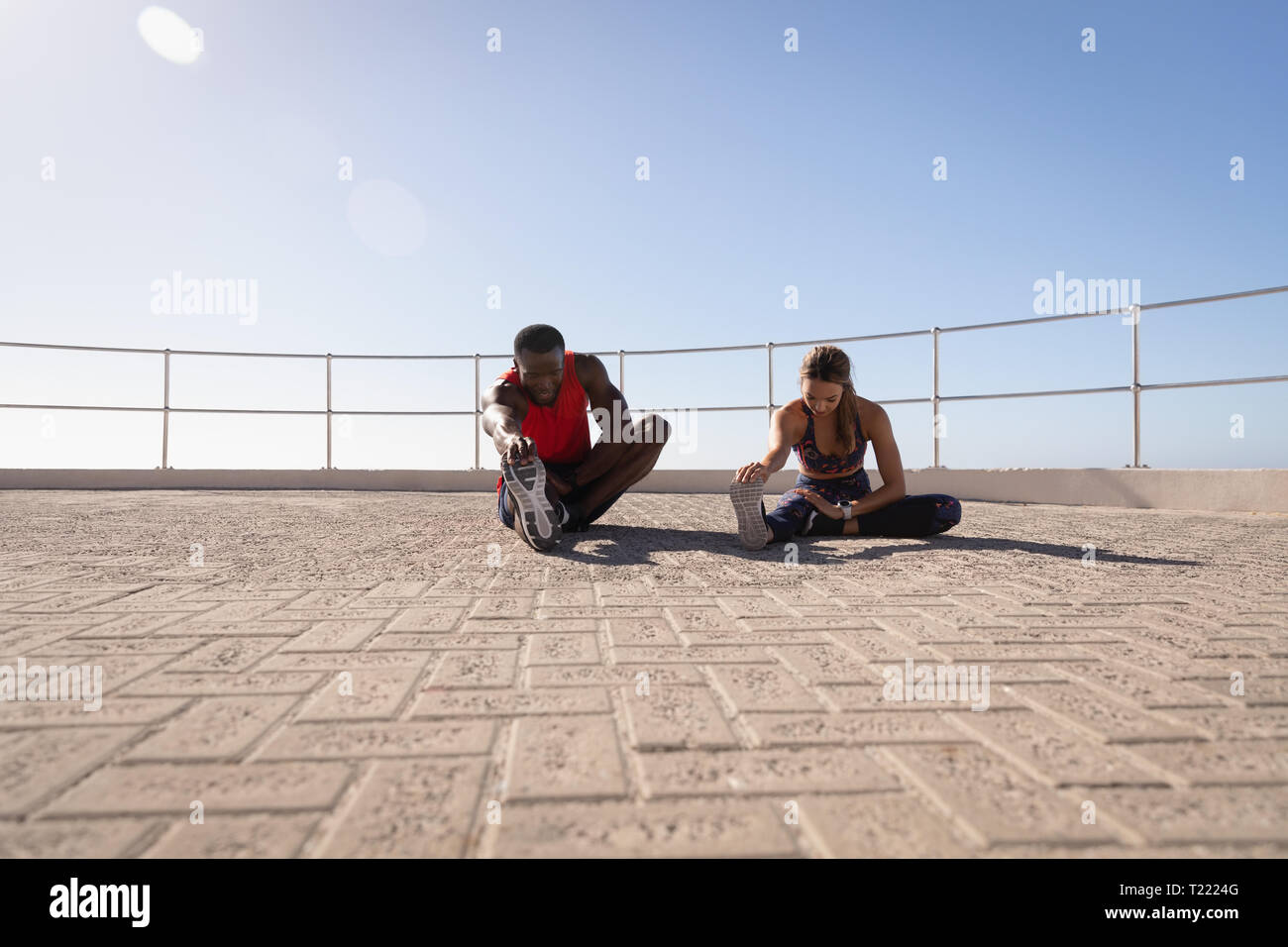 Couple doing stretching exercise on  pavement near promenade beach Stock Photo
