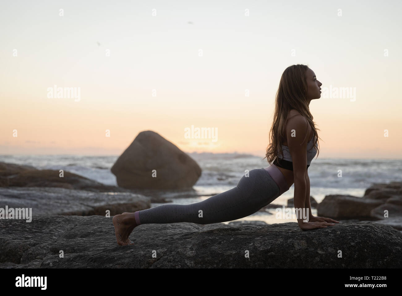 Beautiful woman doing yoga on rock at beach Stock Photo